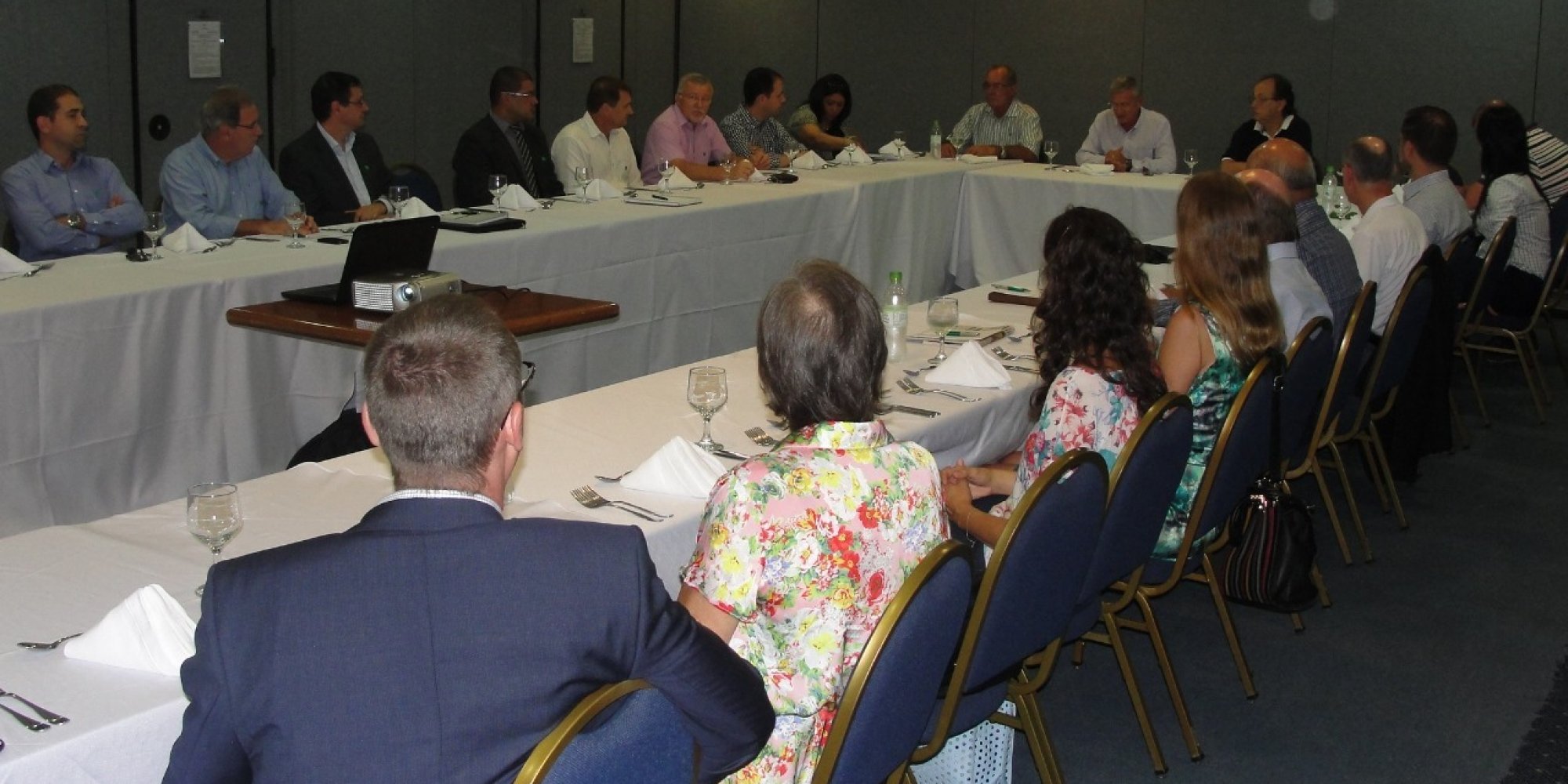 Imagem de mesas em retângulo com com pessoas participando de uma reunião