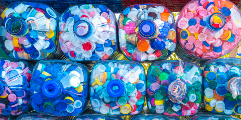 Imagem de nove garrafas de água de plástico empilhadas e cheias de tampas plásticas coloridas dentro 